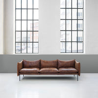 Brown leather sofa with a sleek design, featuring smooth textures against a minimalistic gray wall backdrop.