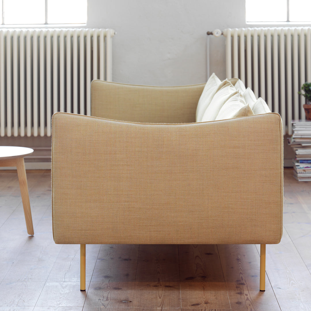 Beige upholstered sofa with a smooth texture and minimalist design, featuring clean lines and wooden legs.