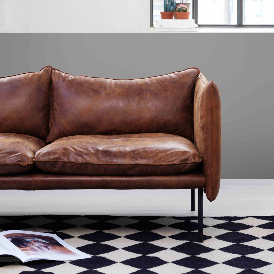 Brown leather sofa on a geometric black and white patterned rug, set against a gray wall.