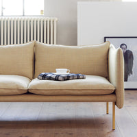 Beige fabric sofa with a smooth texture, featuring a plaid throw blanket and a white cup. Modern minimalist design.