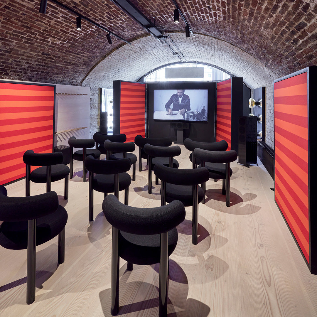 Black chairs with rounded backs, set against vibrant red striped panels and a warm wooden floor. Modern design aesthetic.