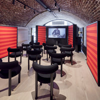 Black chairs with rounded backs, set against vibrant red striped panels and a warm wooden floor. Modern design aesthetic.