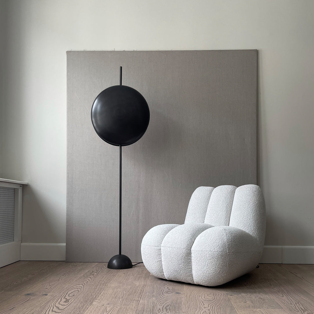 Cozy white boucle chair with soft curves, paired with a sleek black floor lamp against a neutral gray backdrop.