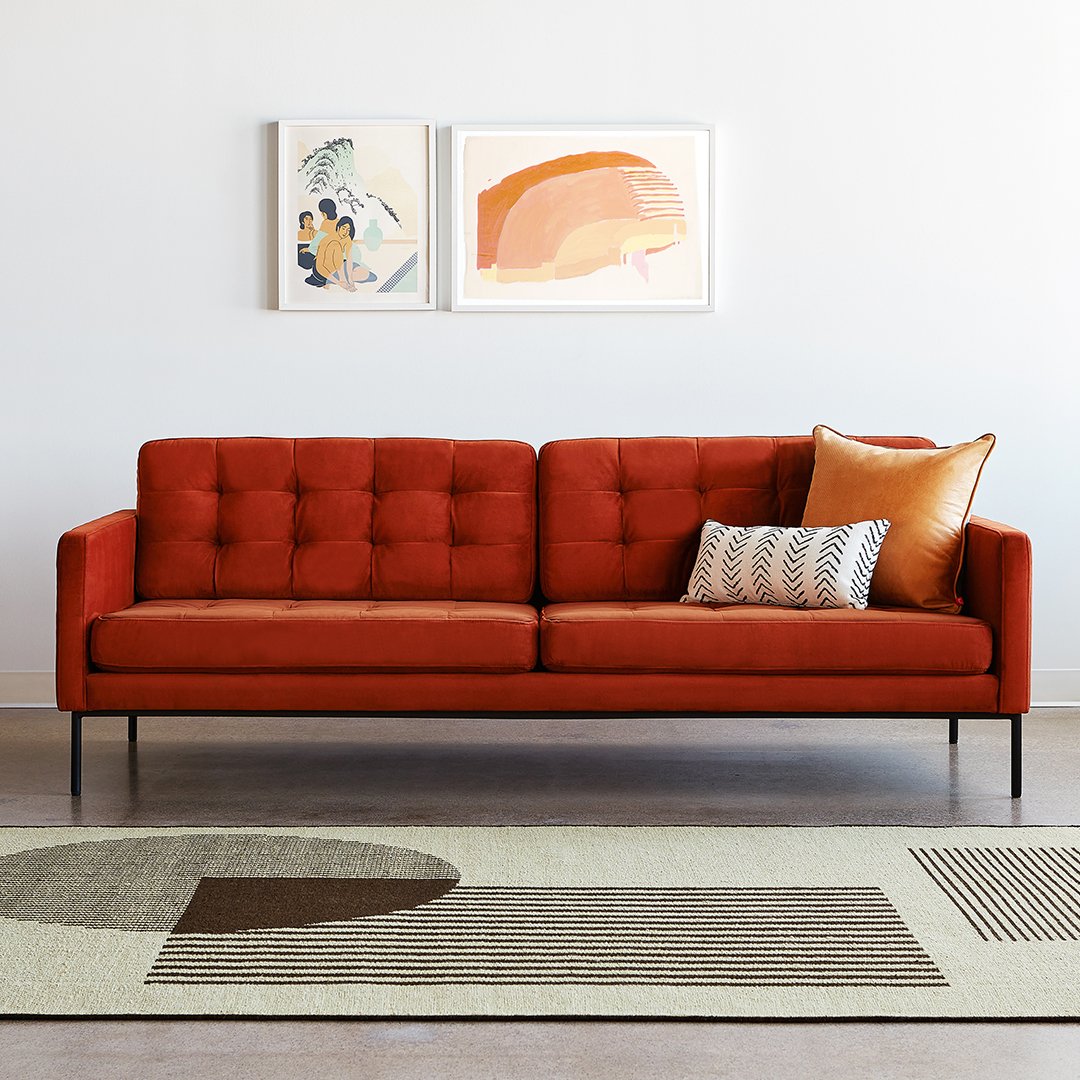 Orange tufted sofa with a geometric rug featuring earth tones and a striped cushion for a modern look.