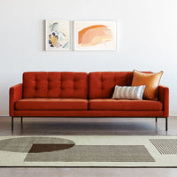 Orange tufted sofa with a geometric rug featuring earth tones and a striped cushion for a modern look.