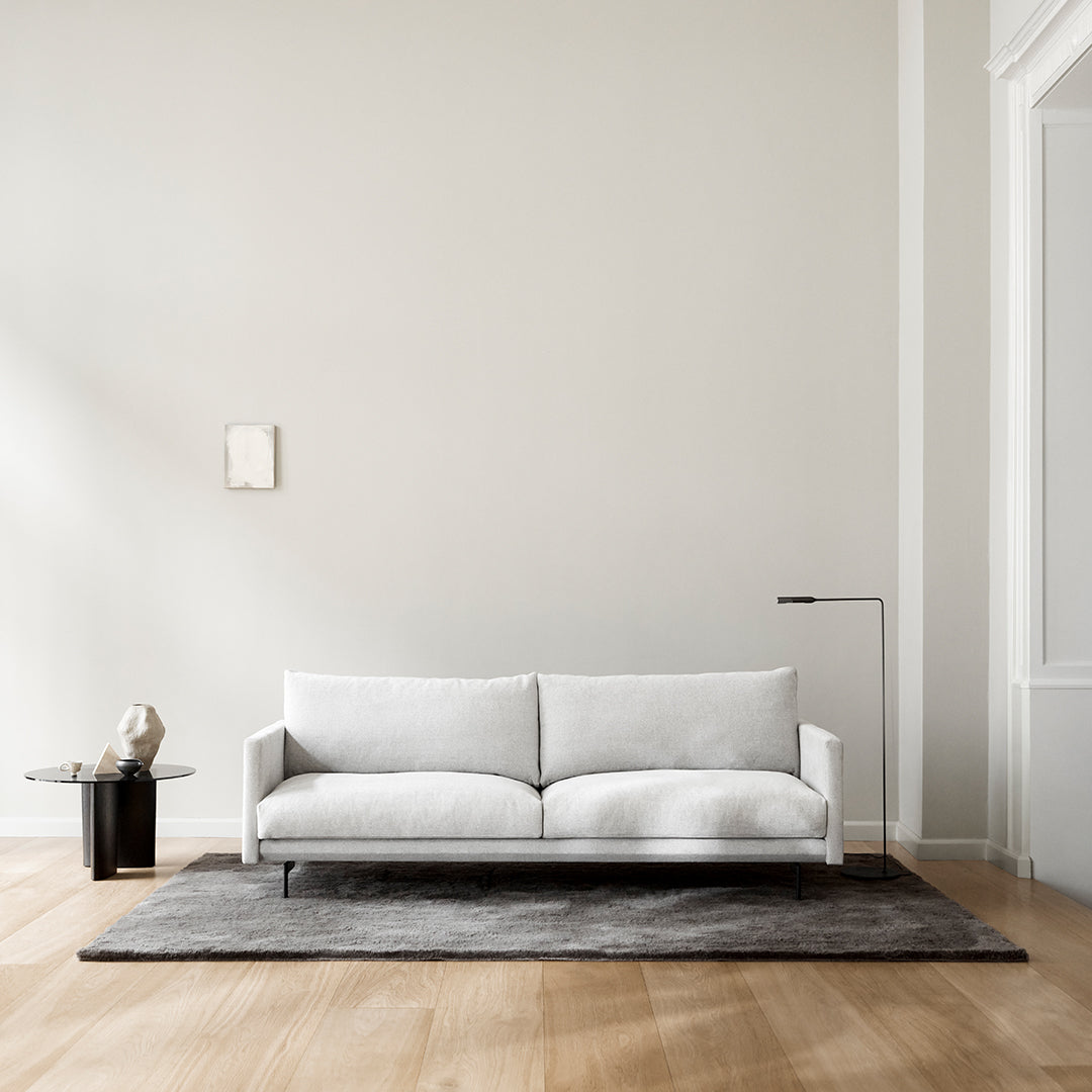 Stylish white sofa on a gray rug, complementing a light wood floor and minimalist decor.