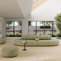Curved green sofa with soft texture, complemented by a matching round ottoman in a modern, airy living space.