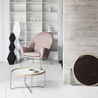 Stylish pink accent chair with a round wooden coffee table and geometric black lamp against a neutral backdrop.