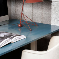 "Stylish blue desk surface with subtle glossy finish, accented by a modern copper lamp and a light beige chair."