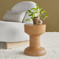 Brown cork accent table with a smooth finish, complemented by a textured gray chair and green plant.