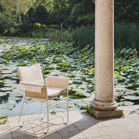 "Neutral beige armchair on a stone patio, surrounded by lush green lily pads and reflections in the water."