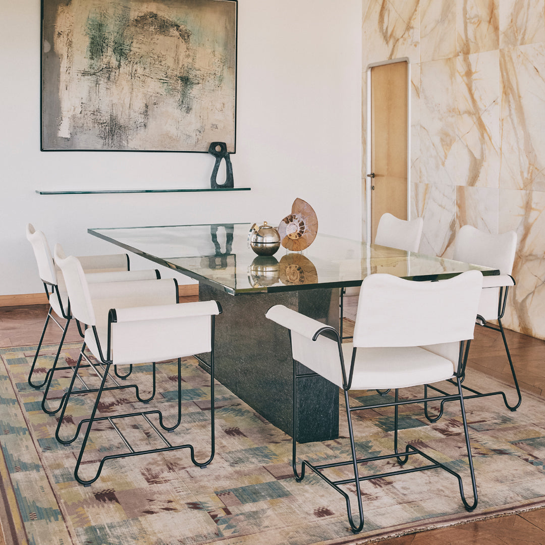 Stylish white chairs on a textured multi-colored rug beneath a glass table in a modern dining room setting.