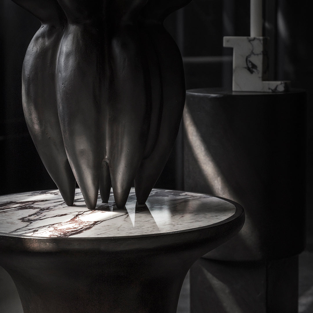 Dark bronze sculpture with marbled white and gray tabletop, softly illuminated with subtle shadows and highlights.