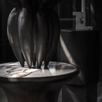 Dark bronze sculpture with marbled white and gray tabletop, softly illuminated with subtle shadows and highlights.