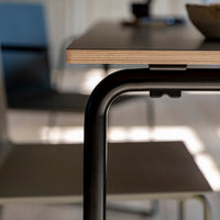 Close-up of a modern table with a light wood finish and sleek black metal legs, against a neutral background.