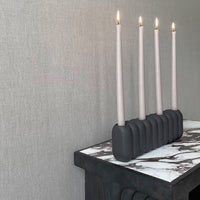 "Elegant gray candle holder with four pale pink candles, set against a textured gray wall and marble tabletop."