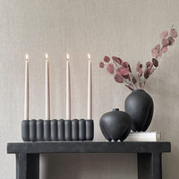 Elegant black candle holder with soft beige candles, paired with a smooth black vase and muted burgundy foliage.