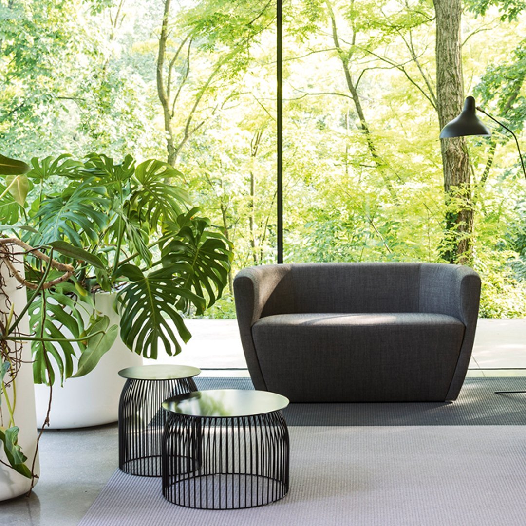 Stylish gray armchair with sleek black wire side tables, set against a vibrant green nature backdrop.