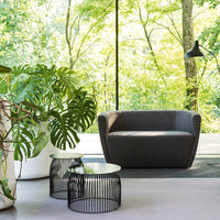 Stylish gray armchair with sleek black wire side tables, set against a vibrant green nature backdrop.