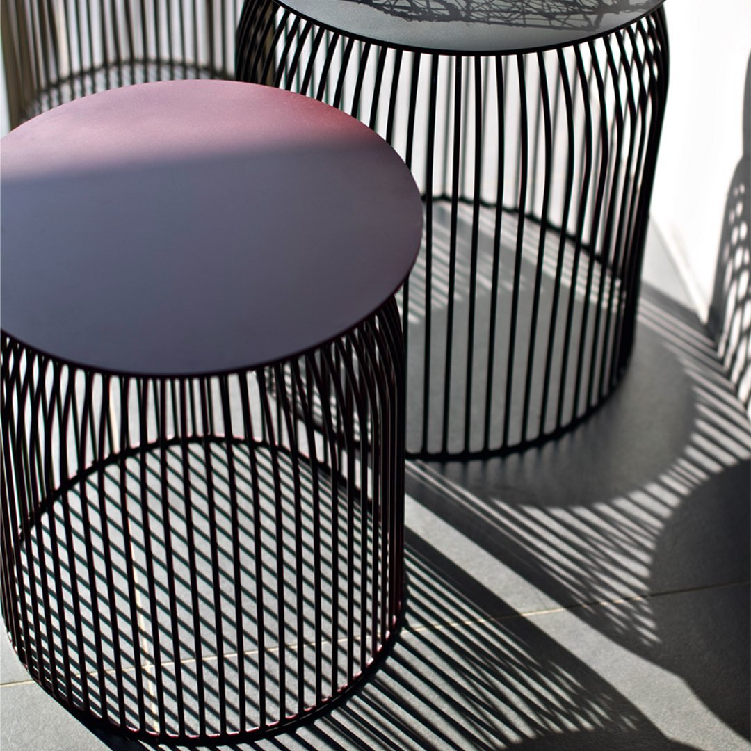 Two modern wire side tables in black with sleek round tops and unique shadow patterns. Ideal for contemporary decor.