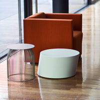 Orange upholstered chair, white round and wire accent tables, modern design, contrasting colors, sleek patterns.