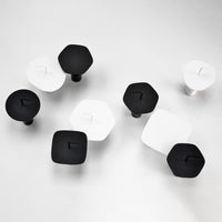 Black and white geometric knobs in square and hexagon shapes, featuring smooth finishes on a light background.