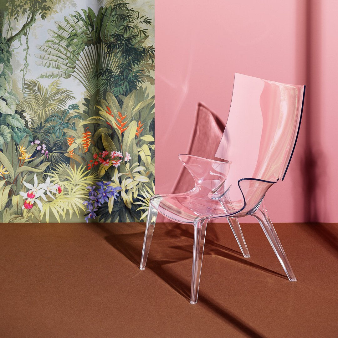 Transparent pink chair against a leafy botanical wallpaper; blend of soft pink, green, and earthy tones.