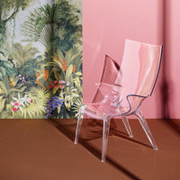 Transparent pink chair against a leafy botanical wallpaper; blend of soft pink, green, and earthy tones.