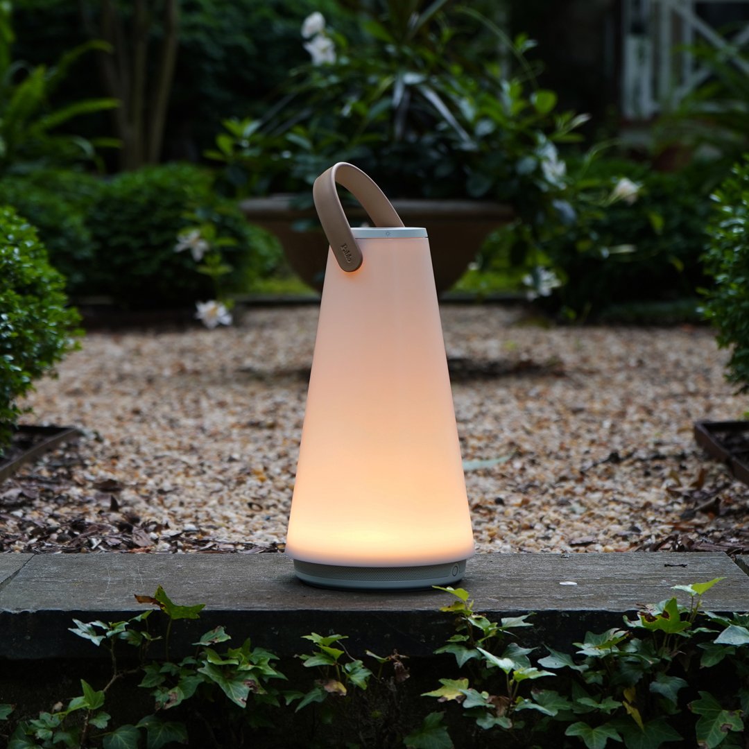 Soft white gradient lantern with a sleek, modern design and a natural wooden handle against a lush garden backdrop.