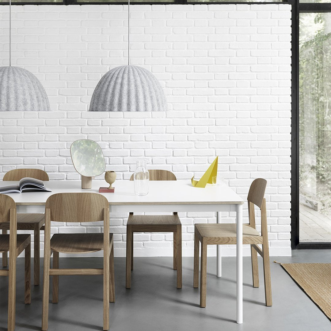 Minimalist dining area features a white table, light wooden chairs, grey pendant lights, and a textured white brick wall.