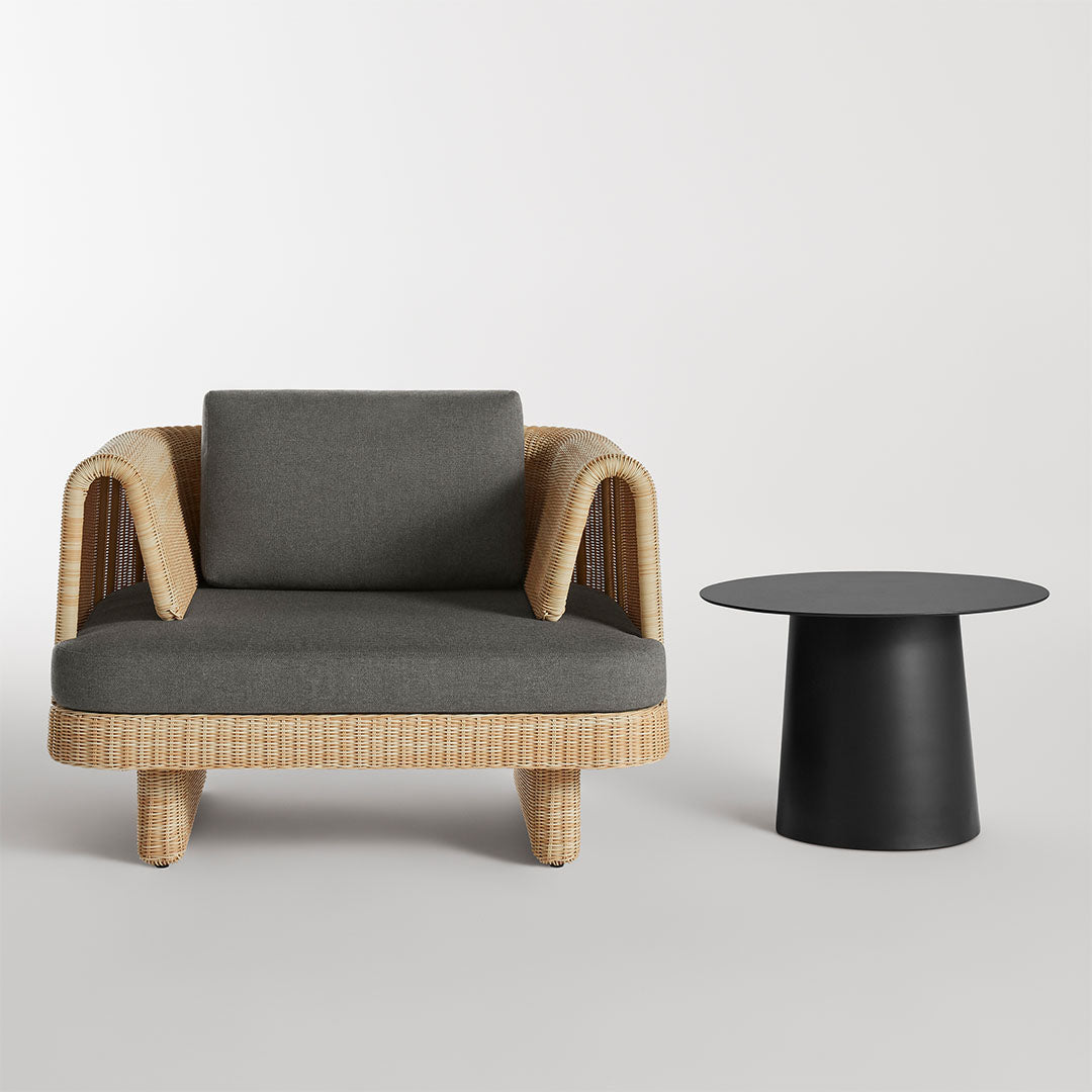 Stylish rattan sofa with a gray cushion, paired with a sleek black round table on a neutral background.