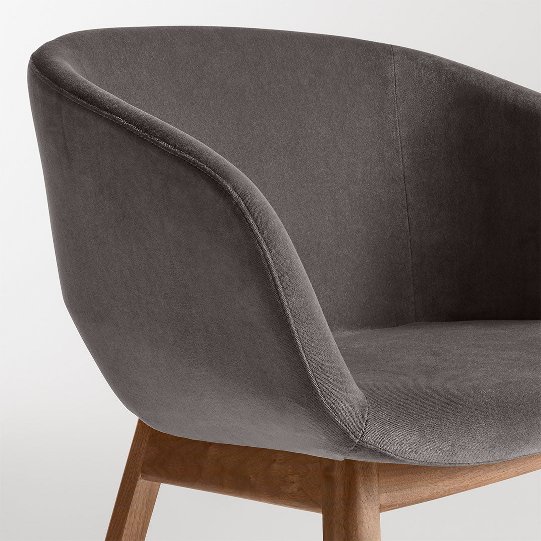 Grey velvet armchair with smooth texture and natural wood legs, featuring a minimalist and modern design.