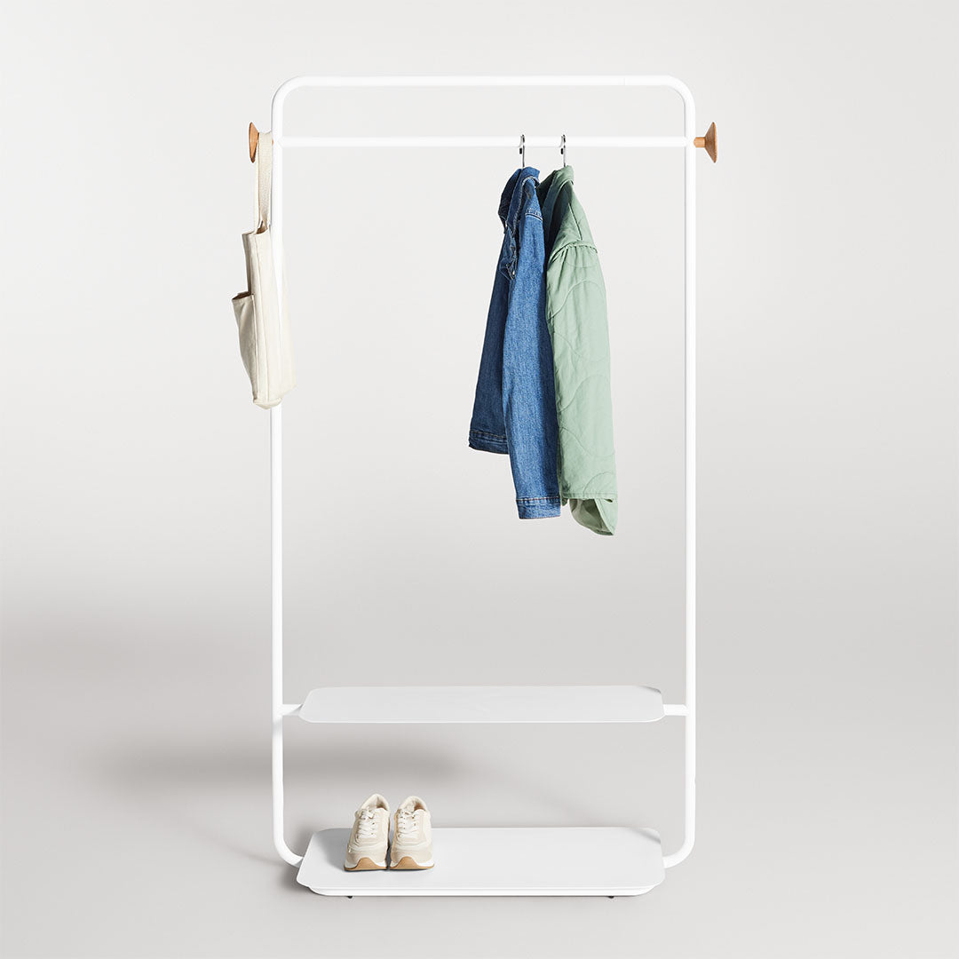 White minimalist clothing rack with blue and green jackets, beige handbag, and white shelves. Clean and modern design.