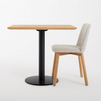 Modern wooden table with a light oak finish and a black metal base, paired with a beige upholstered chair.
