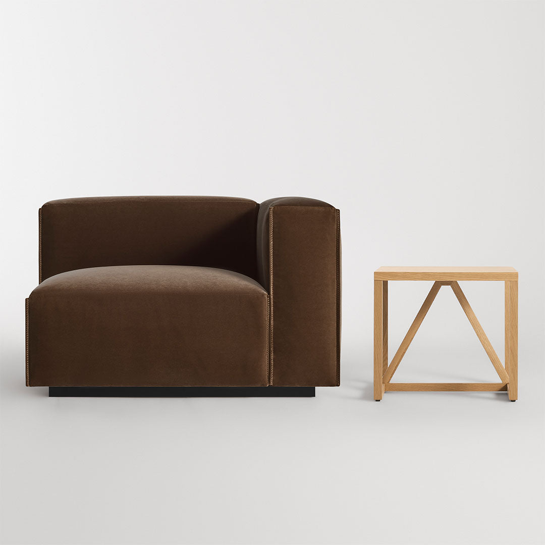 Brown velvet armchair with smooth, modern lines beside a minimalist wooden side table.