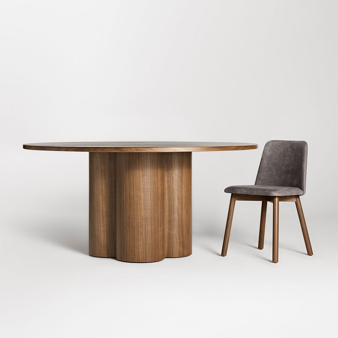 Round wood dining table with a brown finish and a unique scalloped base, paired with a grey upholstered chair.
