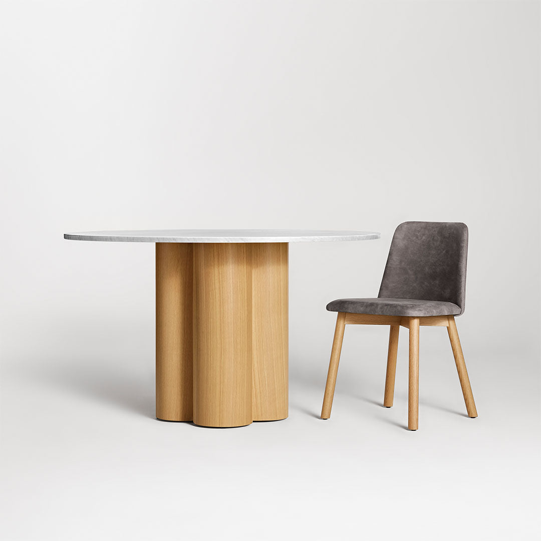 Round table with a wooden base and smooth white top, paired with a plush gray chair featuring light wood legs.