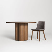 Round wood table with a ribbed base and gray velvet chair, showcasing a modern natural color palette.
