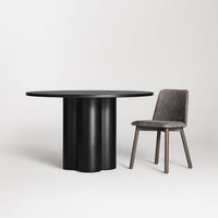 Black round table with a sculpted base, paired with a textured gray chair, creating a modern aesthetic.