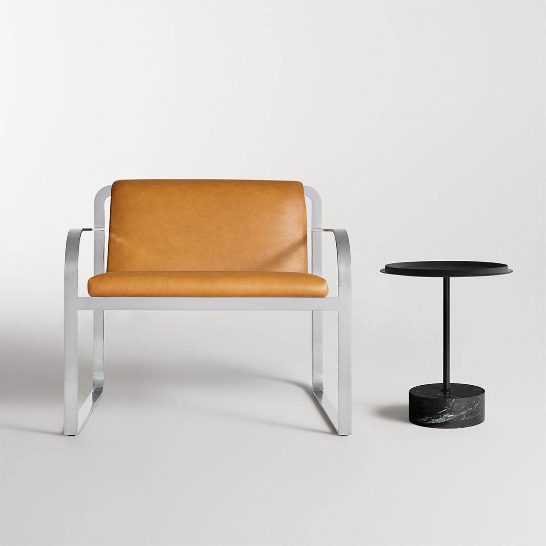 Modern chair with a tan leather seat and sleek silver frame, paired with a round black marble side table.