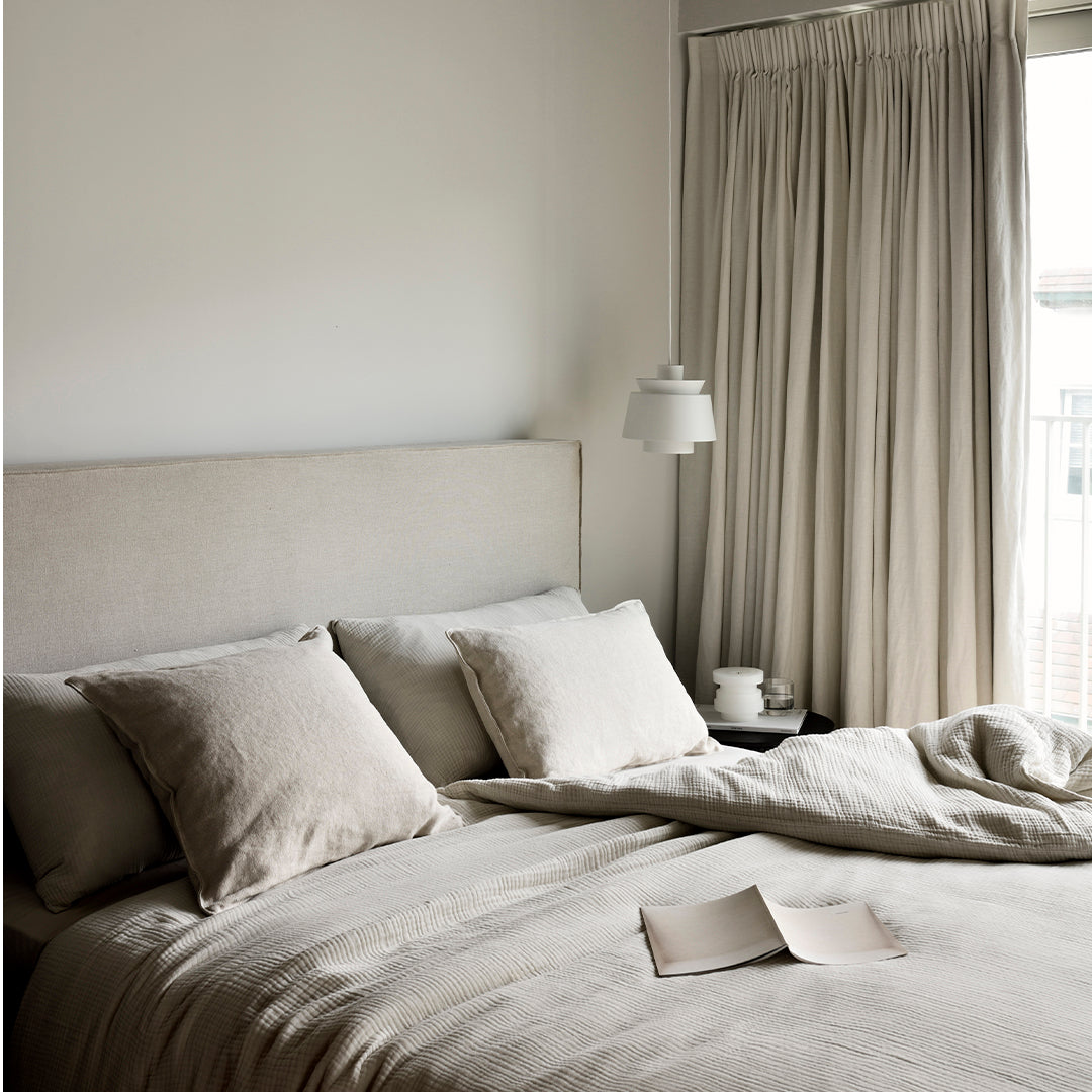 Neutral beige bedding set with textured fabric, paired with soft, flowing curtains in a light, calming hue.