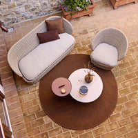 Woven beige sofa and chair with brown cushions on a round brown rug, set against a stone patio.