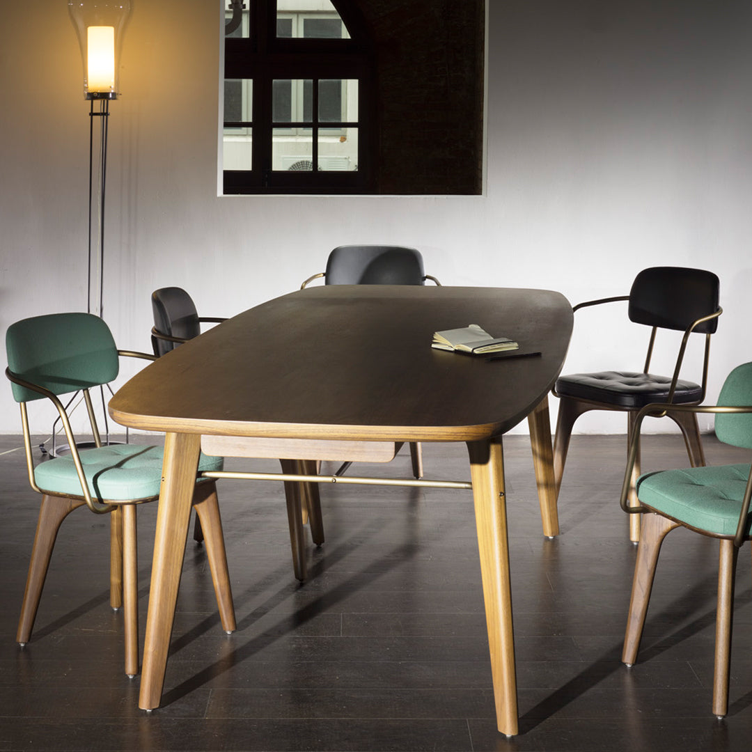 Mid-century modern dining table in natural wood finish with black and green upholstered chairs, set against a neutral backdrop.