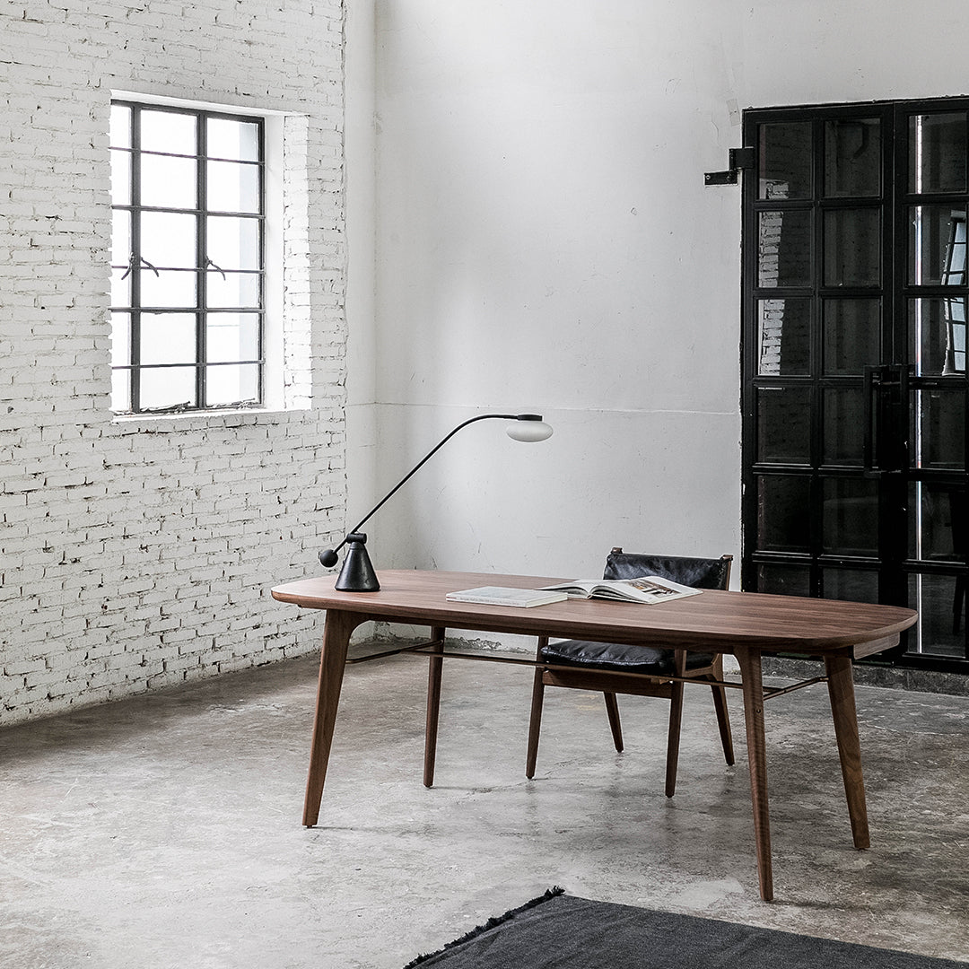 Mid-century walnut desk with sleek lines, complemented by a black chair and minimalistic patterns in a modern interior setting.