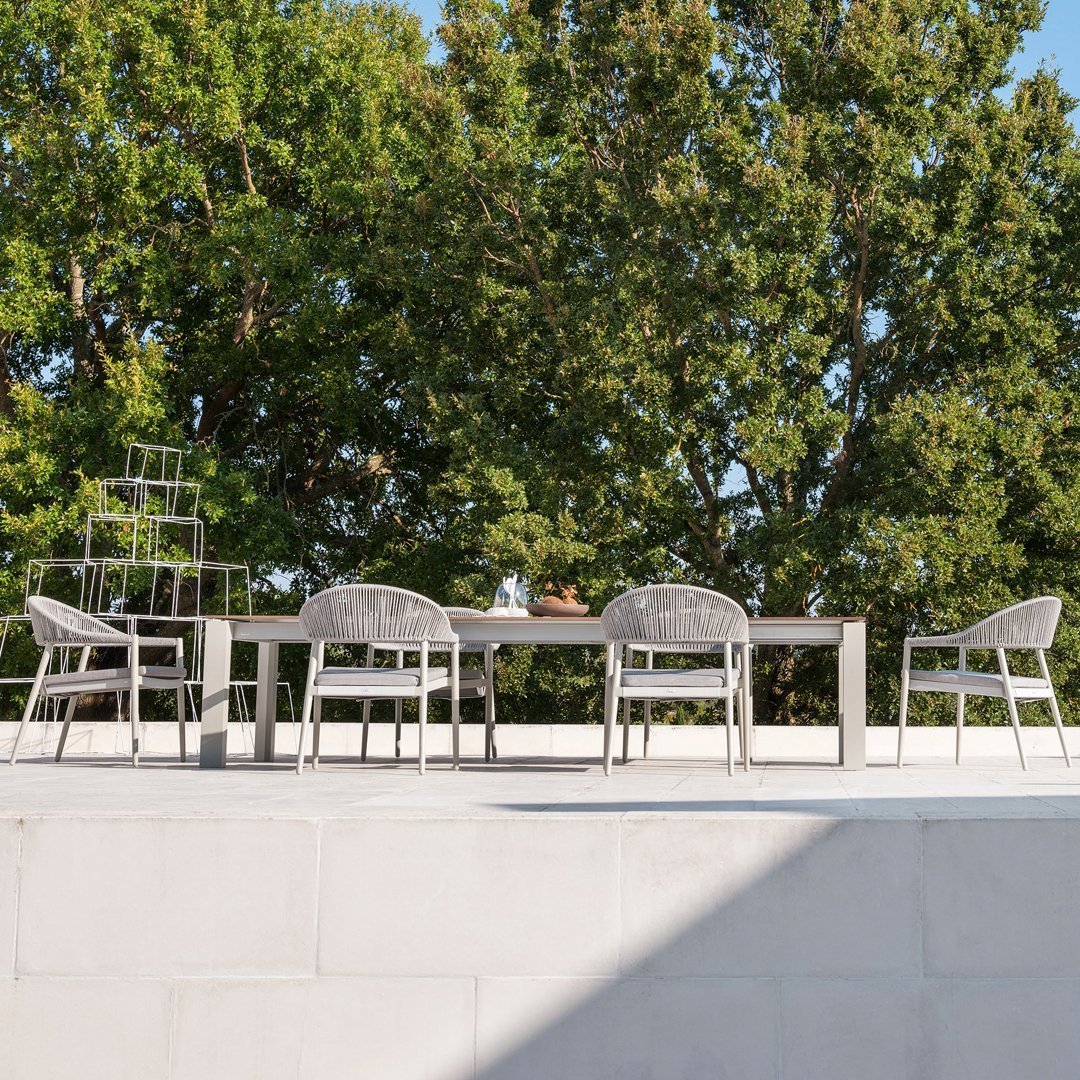 Modern outdoor dining set featuring sleek gray furniture against a backdrop of lush green trees and vibrant sunlight.