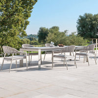 "Elegant outdoor dining set with neutral gray tones and textured woven patterns, set against a lush green backdrop."