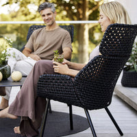 "Black textured chair with a woven pattern, surrounded by greenery and soft earth-toned decor."