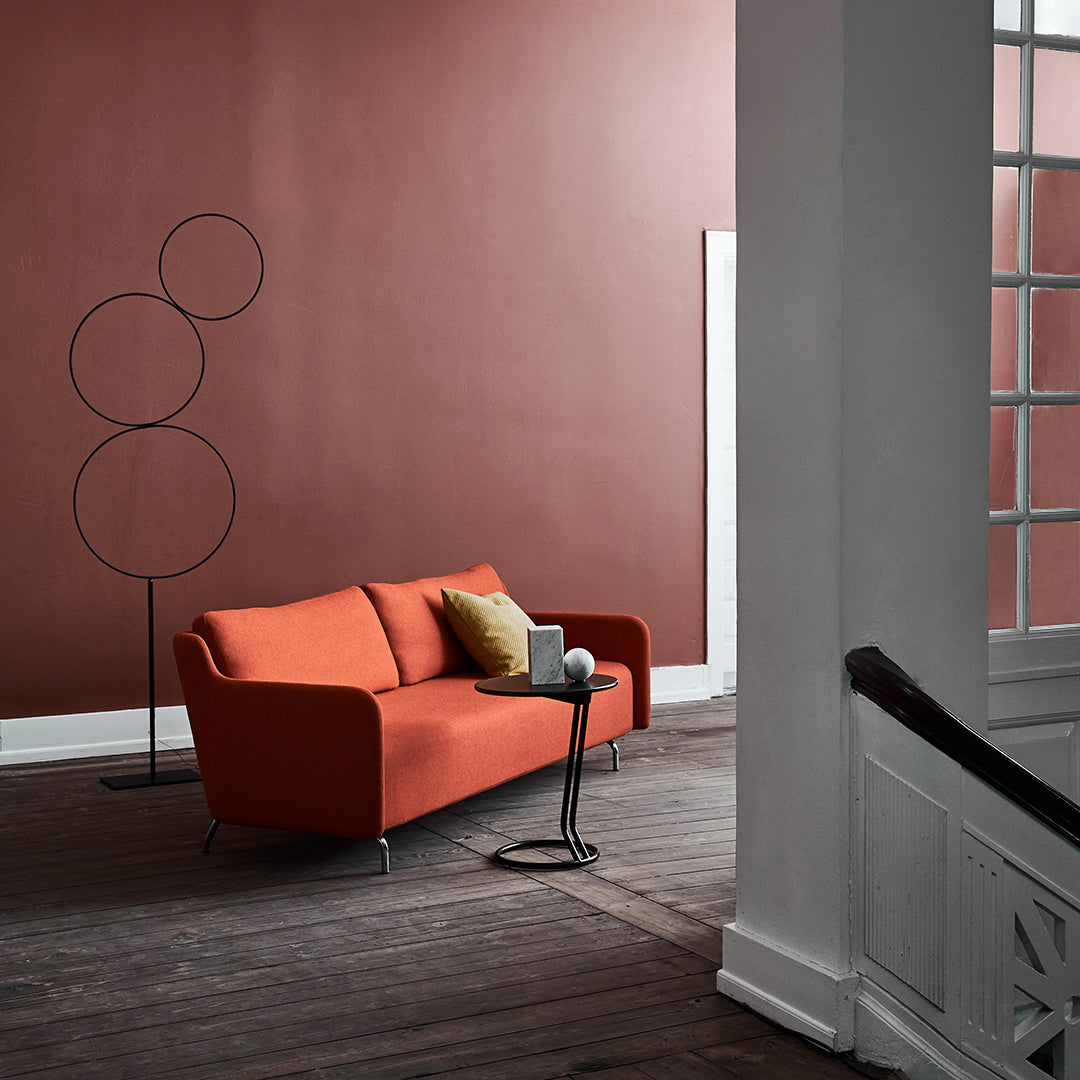 Modern orange sofa with mustard yellow pillow against a deep brown wall, complemented by sleek black and white accents.