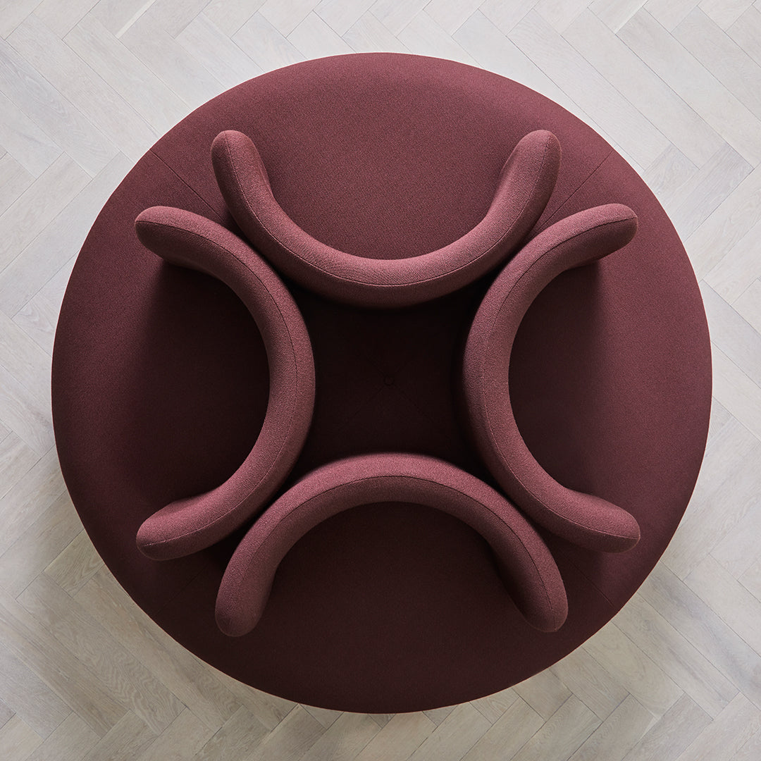Burgundy fabric circular seating with smooth, curved armrests on a light wood floor.