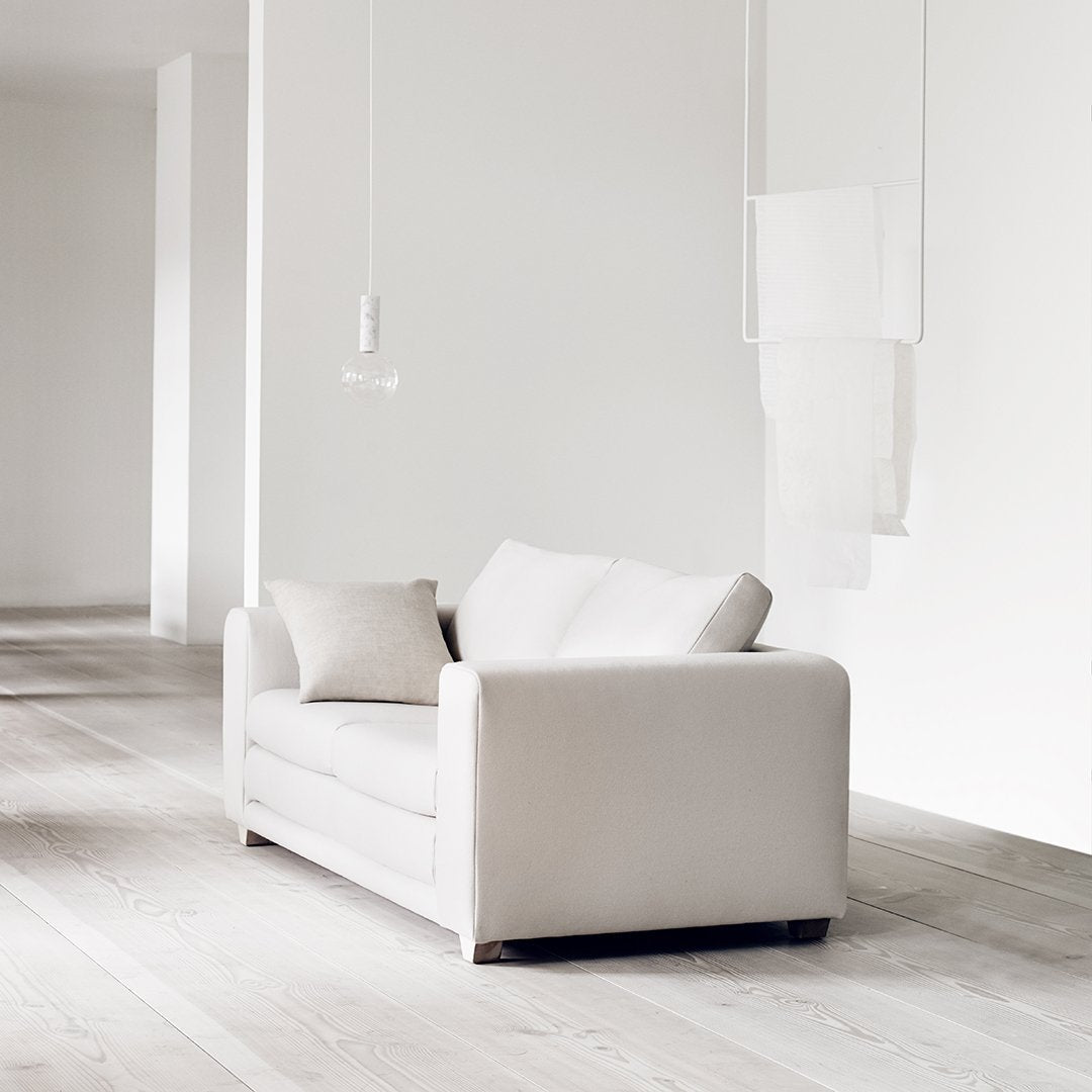 "Soft white sofa with clean lines and a minimalist design, complemented by a light wooden floor."